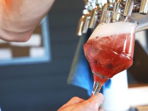 a hot pink sour beer being poured into a stemmed glass from OG bottle shop in galt